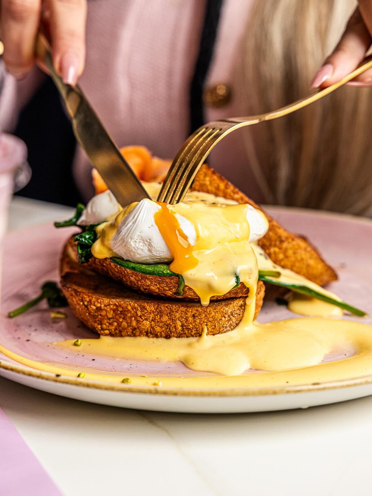 Knife and fork cutting into eggs benedict, the yolk and hollandaise running over the toast