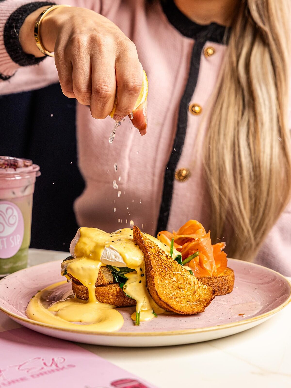 Eggs benedict on toasted brioche with smoked salmon, spinach and hollandaise, being finished with a pinch of seasoning