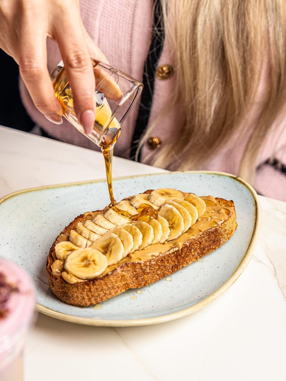 Honey being poured over peanut butter and sliced banana on thick sourdough toast