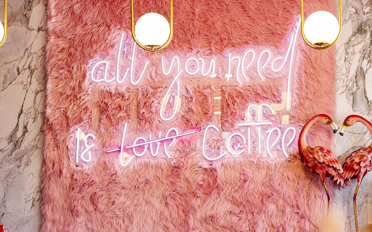 Soft Sip's soft pink interior with velvet booths and the neon 'all you need is coffee' sign