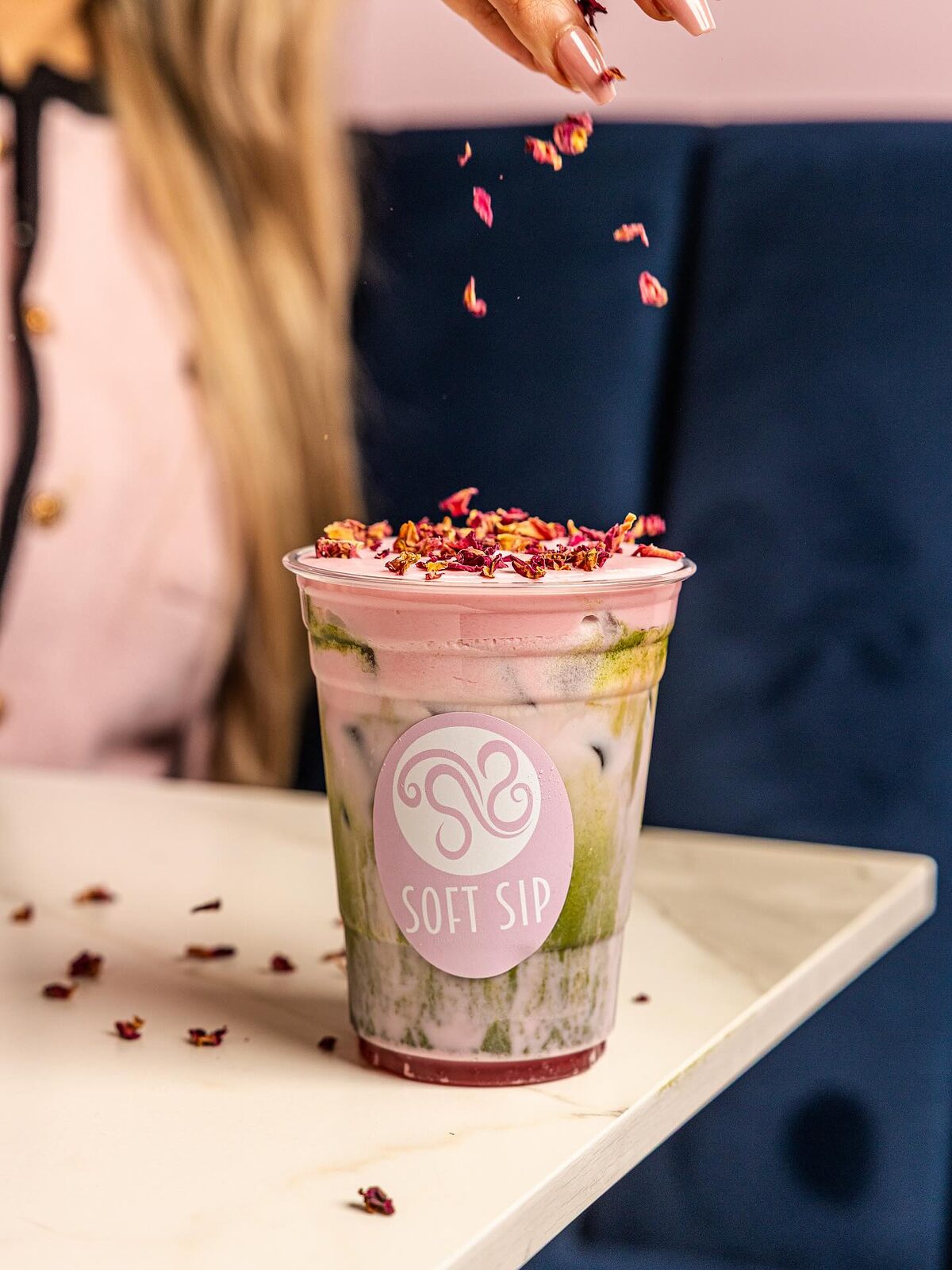 Dried rose petals falling onto a layered pink and green rose cream matcha in a Soft Sip cup