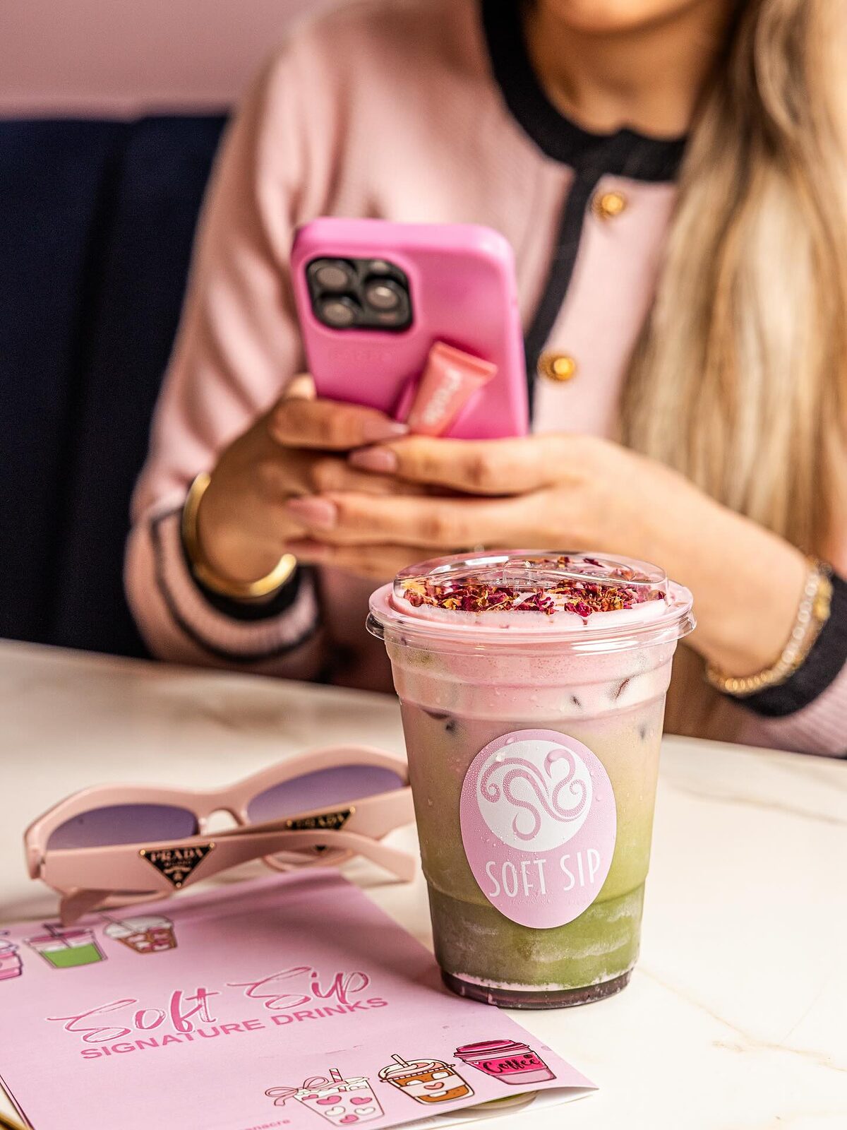 A customer photographing her rose matcha next to the Soft Sip signature drinks menu card