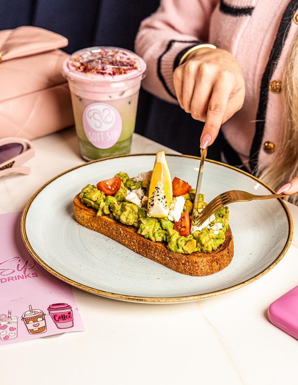 Smashed avocado on sourdough with feta, cherry tomatoes and a lemon wedge on a blue plate